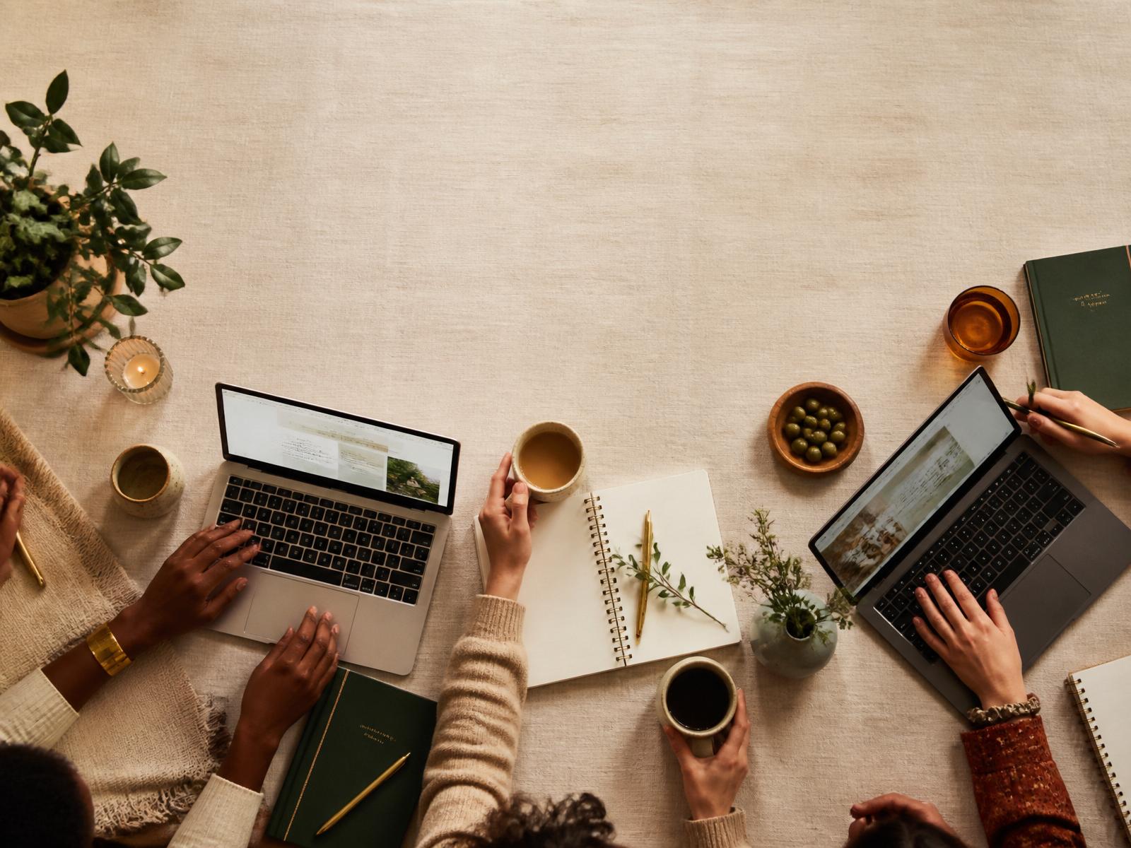 Overhead view of a team collaborating around a warm workspace with laptops, notebooks, and coffee.